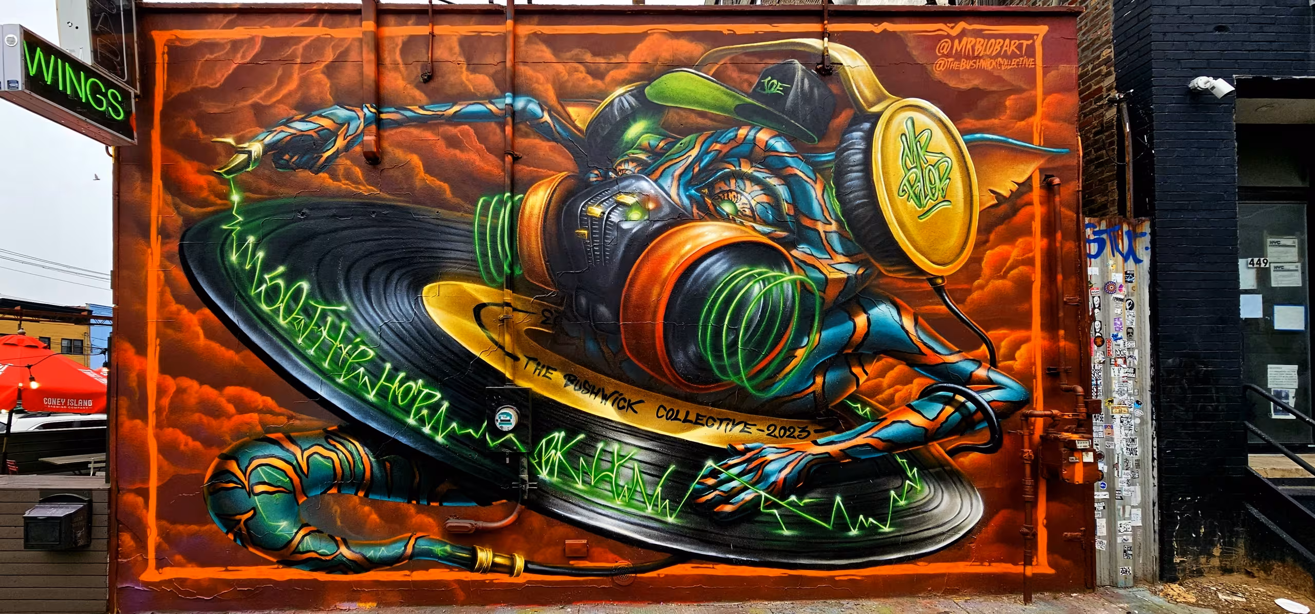 Epic cyberpunk DJ graffiti mural by Italian artist Mr Blob at The Bushwick Collective in Brooklyn, New York, featuring a futuristic character with neon headphones scratching a giant vinyl record.