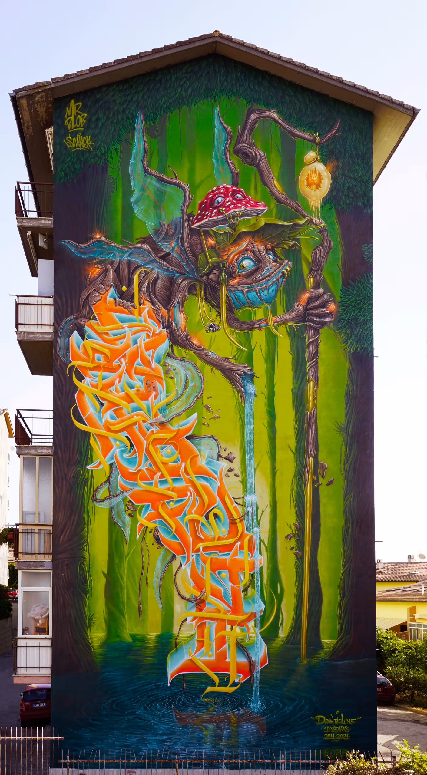 Massive vertical graffiti mural by Mr Blob featuring a surreal forest fantasy creature with a mushroom hat and fairy wings interwoven with giant orange and yellow wildstyle lettering on a building facade.