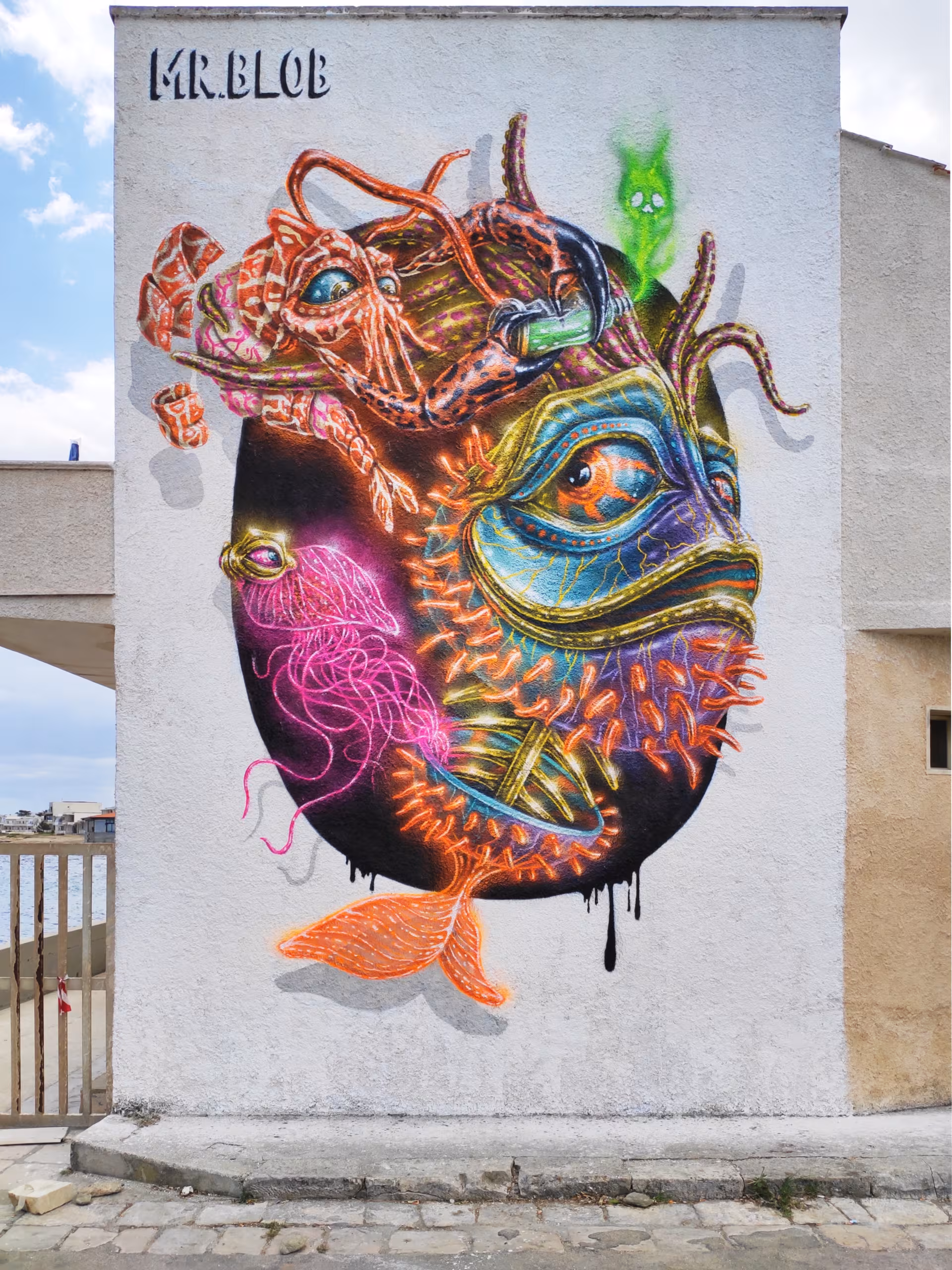 Stunning vertical bio-organic street art mural by Mr Blob, showcasing a surreal deep-sea fish with glowing neon pink jellyfish and an orange crustacean inside a floating dark oval shape.
