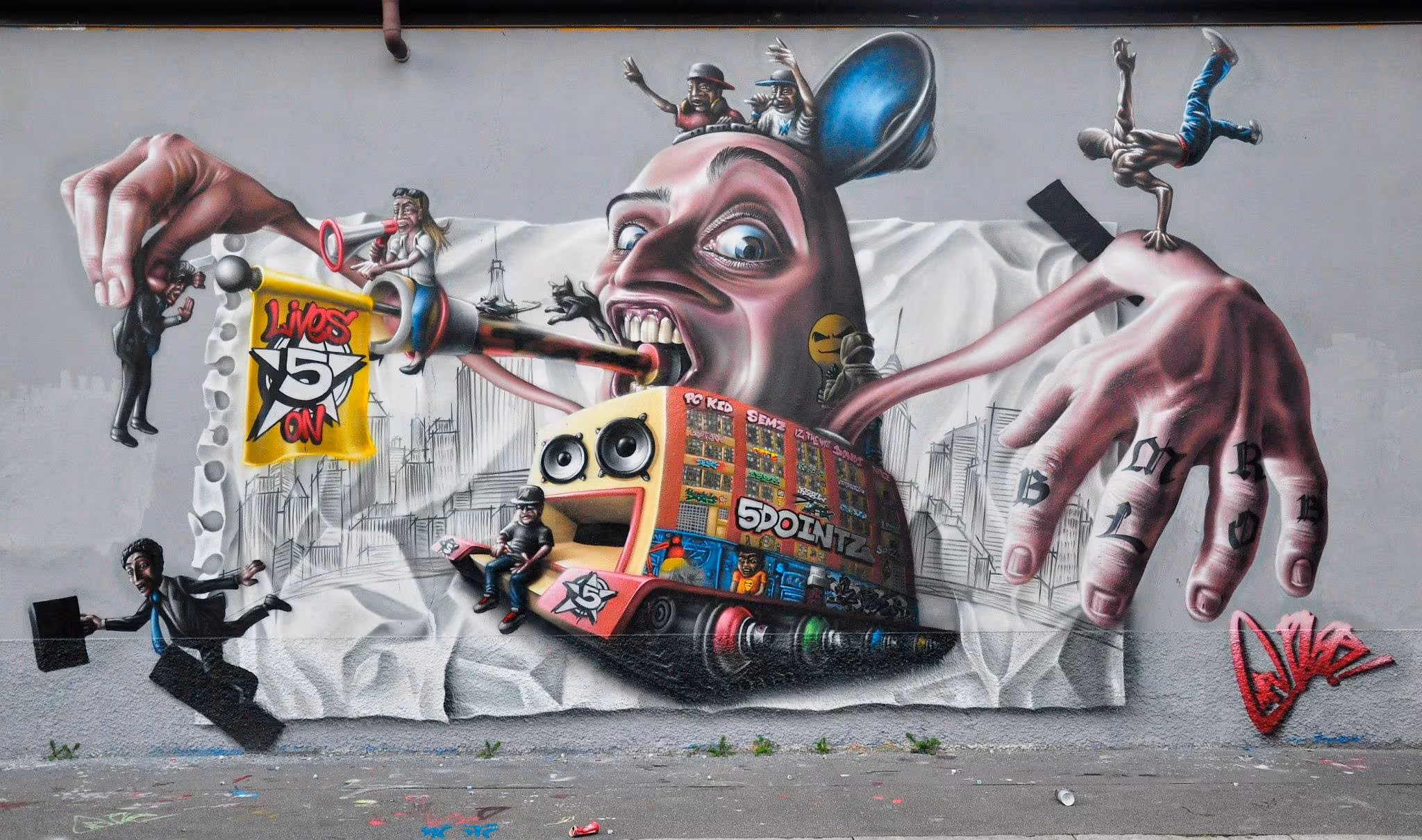 Stunning 3D tribute graffiti mural to New York 5Pointz by Mr Blob, featuring the iconic building turned into a boombox truck, breakdancers, corporate businessmen, and a 5 Lives On flag on a torn paper background.