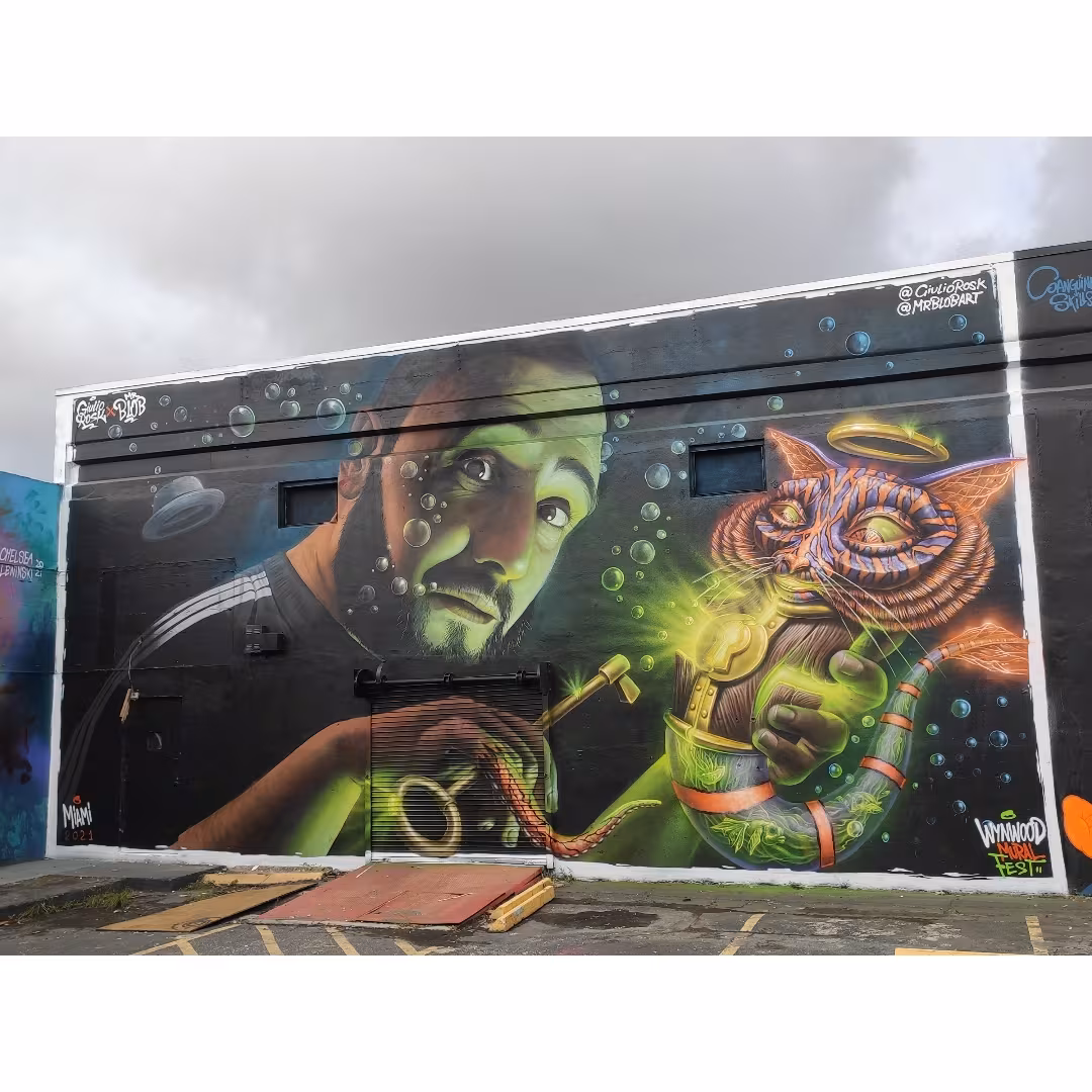 Stunning collaborative graffiti mural by Mr Blob and Giulio Rosk at Wynwood Mural Fest in Miami, featuring a realistic male portrait underwater and a surreal neon cat character.